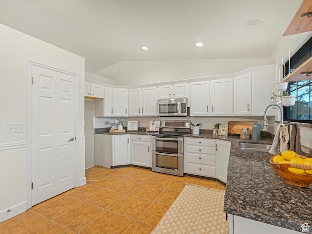 kitchen featuring lofted ceiling, white cabinetry, stainless steel appliances, and a sink