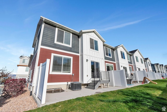 rear view of property with board and batten siding, a yard, central air condition unit, and a patio