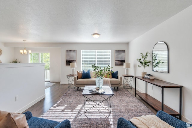 living area with wood finished floors, a textured ceiling, baseboards, and a notable chandelier