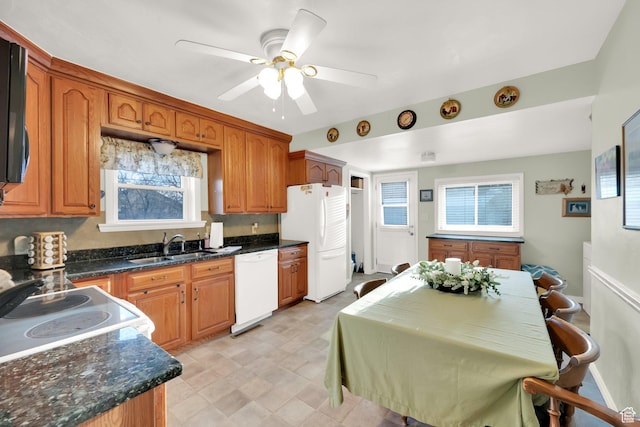kitchen featuring brown cabinets, dark stone countertops, a ceiling fan, a sink, and white appliances