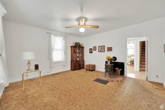 living area with carpet floors, a wood stove, ceiling fan, and visible vents