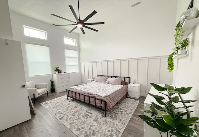 bedroom featuring wainscoting, wood finished floors, visible vents, and a decorative wall