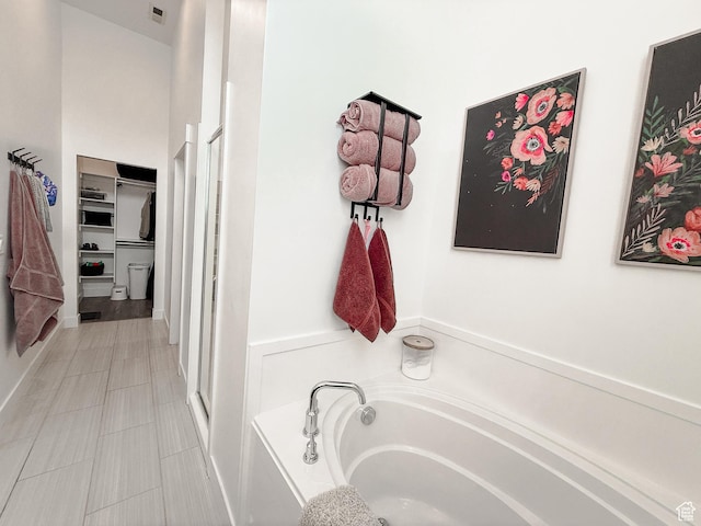 bathroom featuring a bath, a walk in closet, visible vents, and a stall shower