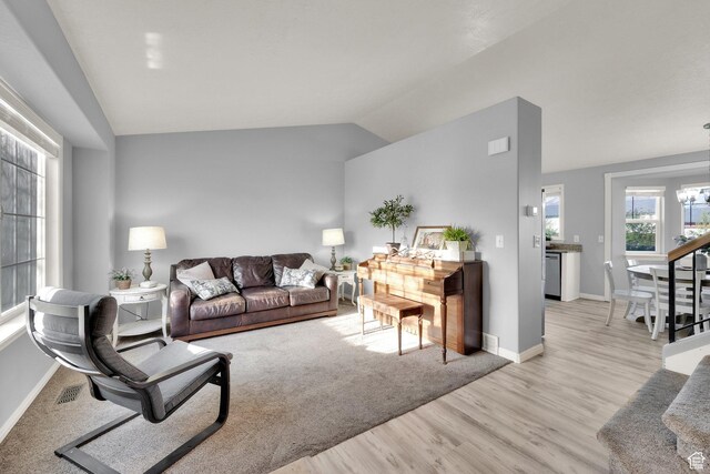living room with vaulted ceiling, light wood finished floors, baseboards, a notable chandelier, and visible vents