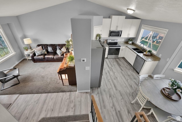 kitchen featuring white cabinets, a sink, light wood-type flooring, lofted ceiling, and appliances with stainless steel finishes