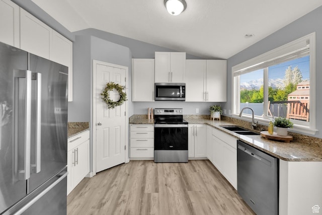 kitchen featuring lofted ceiling, stainless steel appliances, a sink, and light wood finished floors