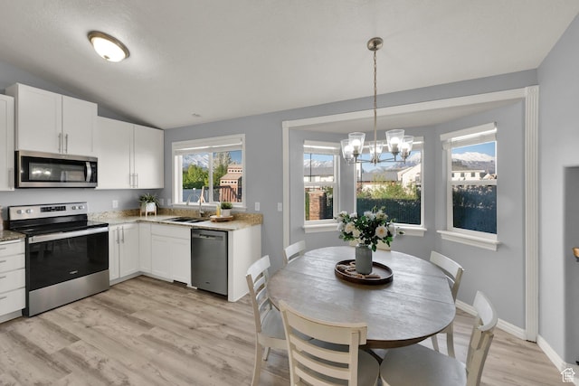 kitchen with vaulted ceiling, a sink, light wood-style floors, appliances with stainless steel finishes, and white cabinetry