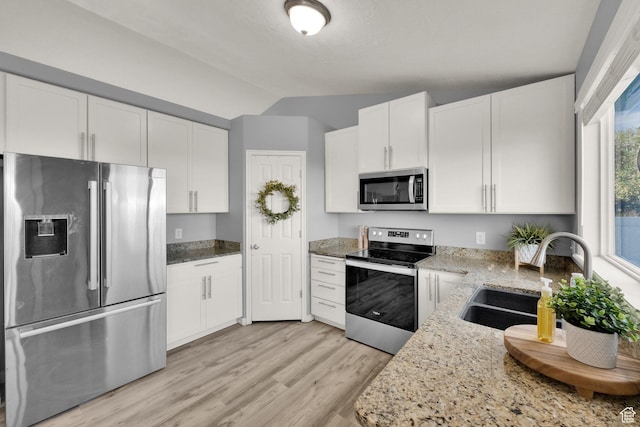 kitchen with stainless steel appliances, a sink, light wood-type flooring, vaulted ceiling, and light stone counters