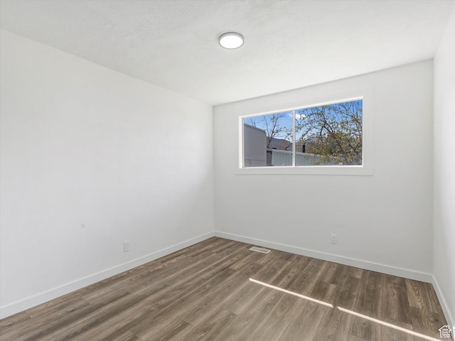 spare room featuring wood finished floors, visible vents, and baseboards