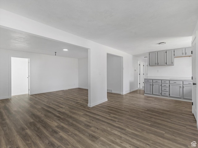 unfurnished living room with baseboards, visible vents, and dark wood-style floors