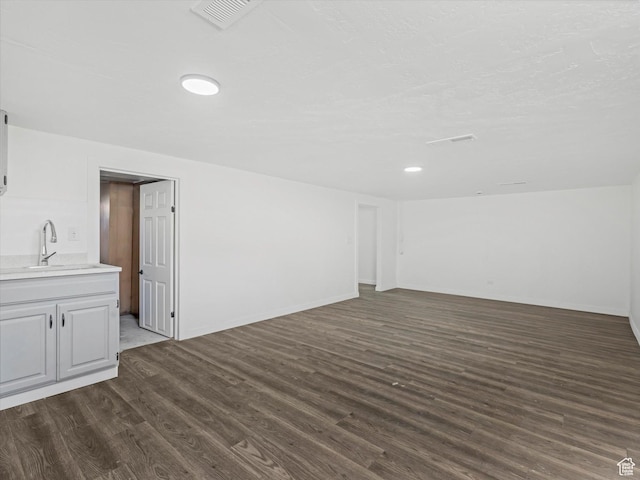 below grade area featuring dark wood finished floors, visible vents, and a sink