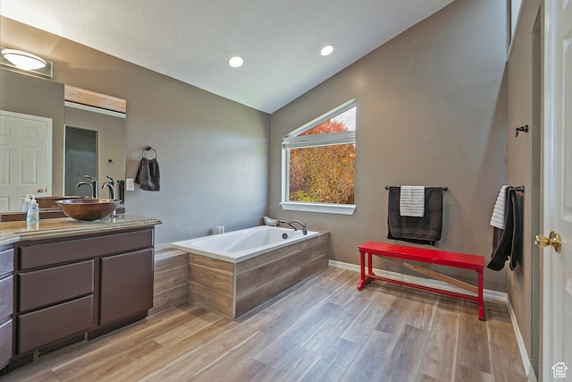 bathroom featuring a bath, vaulted ceiling, baseboards, wood finished floors, and vanity