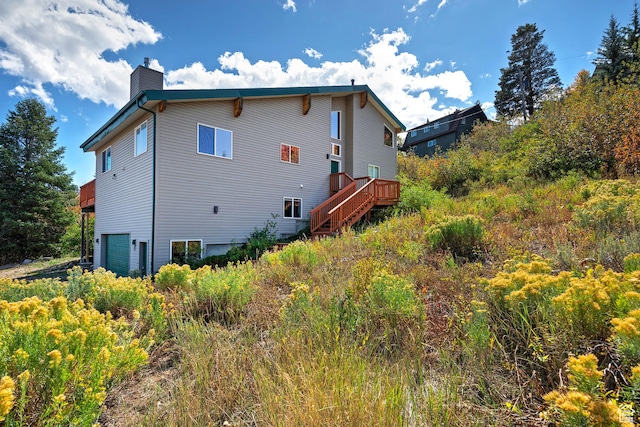 rear view of property featuring a chimney, an attached garage, a deck, and stairs
