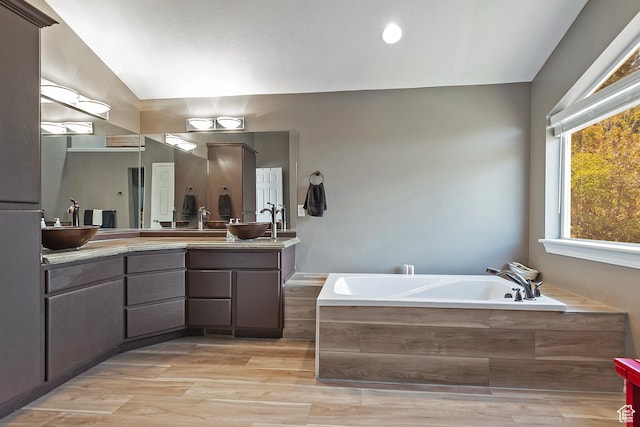 bathroom featuring vaulted ceiling, a garden tub, wood finished floors, a sink, and double vanity