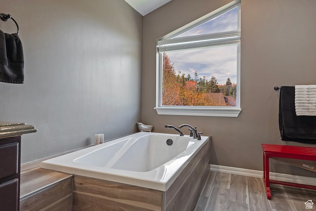 full bath with wood finished floors, a garden tub, and baseboards