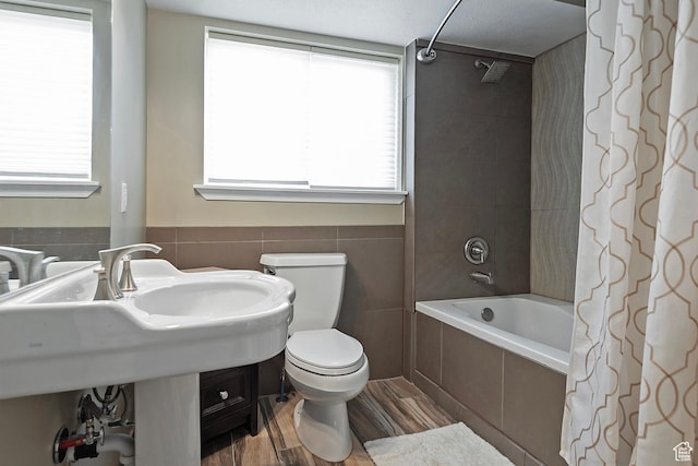 full bathroom featuring tiled shower / bath combo, wood finished floors, a healthy amount of sunlight, and toilet