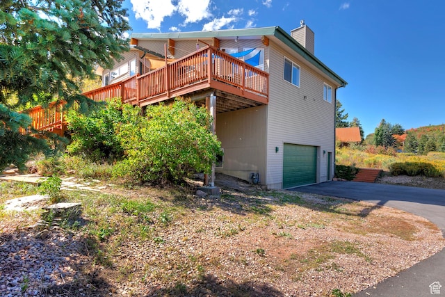 back of property featuring an attached garage, a wooden deck, a chimney, and aphalt driveway