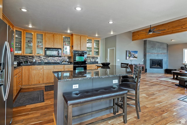 kitchen featuring light wood finished floors, a kitchen breakfast bar, decorative backsplash, a ceiling fan, and black appliances