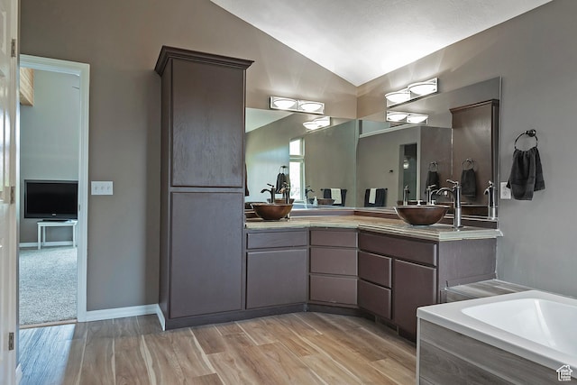 bathroom featuring lofted ceiling, wood finished floors, a sink, and double vanity