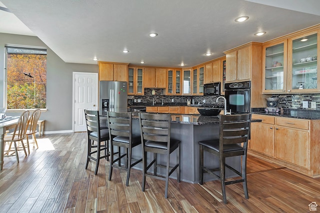 kitchen featuring tasteful backsplash, recessed lighting, glass insert cabinets, wood finished floors, and black appliances
