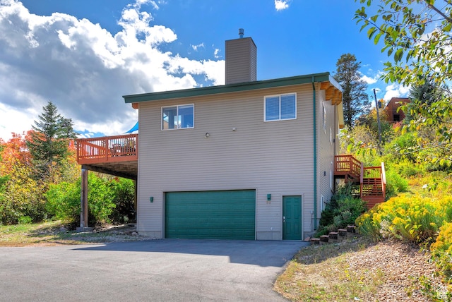 back of house with a chimney, driveway, a deck, a garage, and stairs