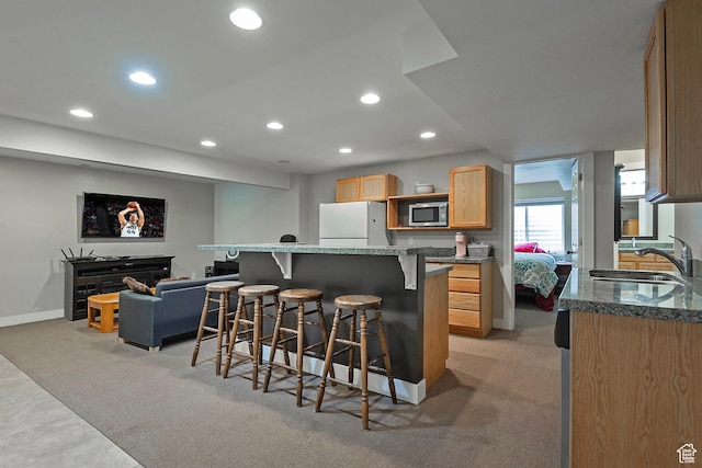 kitchen with a sink, stainless steel microwave, freestanding refrigerator, recessed lighting, and light colored carpet