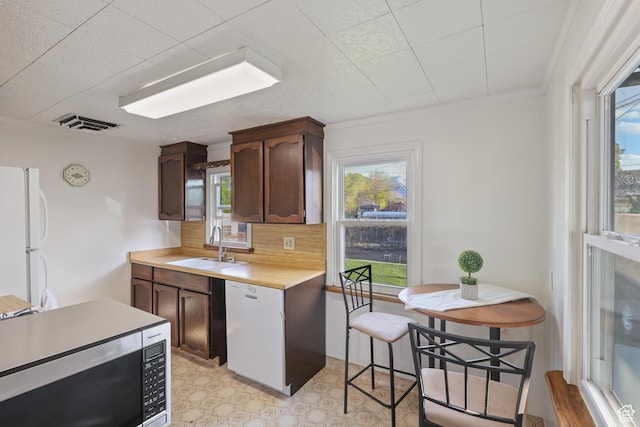 kitchen featuring light countertops, backsplash, a sink, white appliances, and crown molding