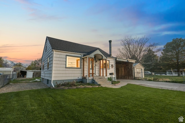 bungalow-style home featuring concrete driveway, a carport, fence, an outbuilding, and a yard