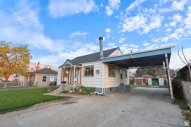 bungalow-style home with a storage shed, driveway, fence, an attached carport, and a front yard