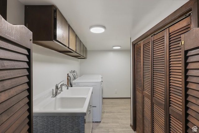 clothes washing area featuring baseboards, a sink, light wood-style floors, and independent washer and dryer