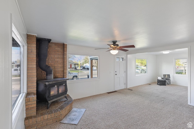 living area featuring a healthy amount of sunlight, a wood stove, and carpet