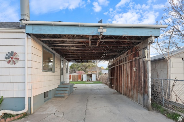 view of parking / parking lot featuring fence, an attached carport, and a storage shed