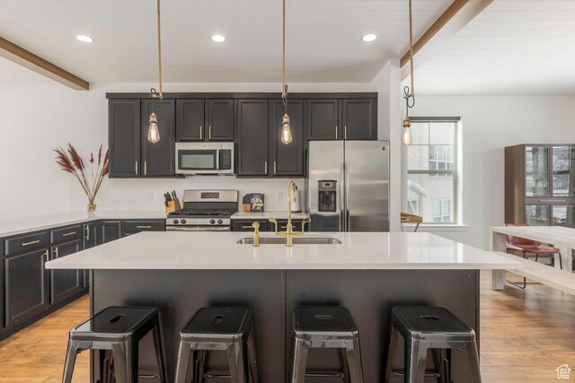 kitchen with a sink, stainless steel appliances, light wood finished floors, light countertops, and a kitchen bar