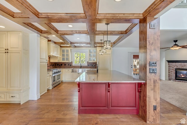 kitchen with light stone counters, a ceiling fan, a sink, beamed ceiling, and range with two ovens