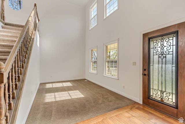 carpeted foyer entrance featuring stairway, a towering ceiling, baseboards, and wood finished floors