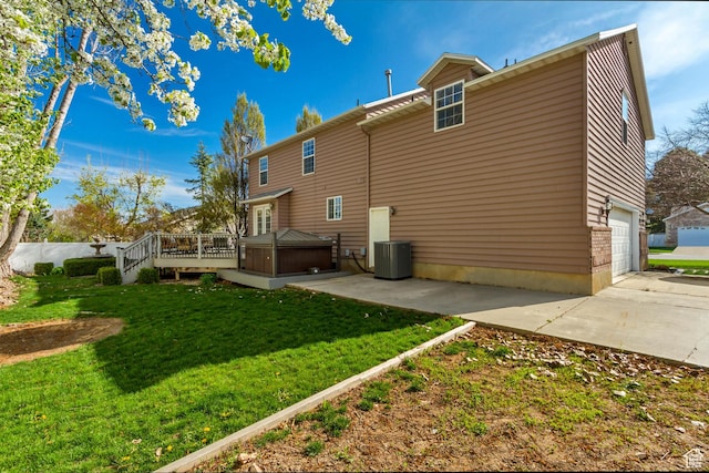 rear view of house featuring a jacuzzi, central AC, concrete driveway, a lawn, and a deck