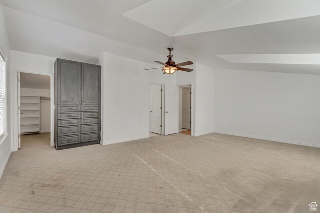 unfurnished bedroom with a walk in closet, ceiling fan, light carpet, baseboards, and lofted ceiling