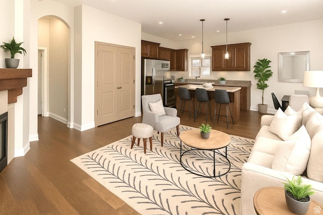 living area with arched walkways, baseboards, recessed lighting, a fireplace, and dark wood-type flooring
