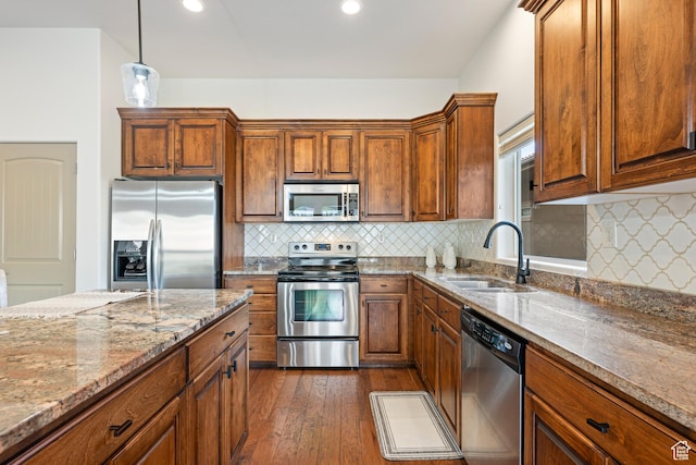 kitchen with stainless steel appliances, a sink, dark wood finished floors, light stone countertops, and brown cabinetry