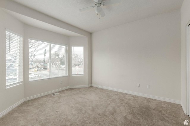 spare room featuring light colored carpet, baseboards, a ceiling fan, and visible vents