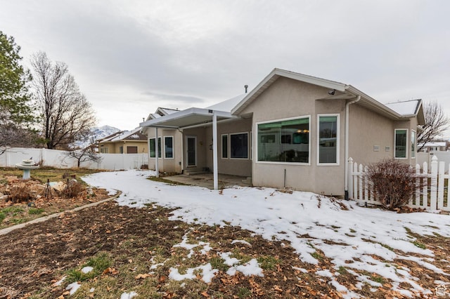 snow covered rear of property with fence and stucco siding