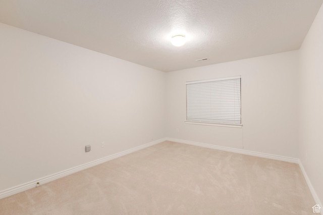 spare room with light colored carpet, baseboards, a textured ceiling, and visible vents
