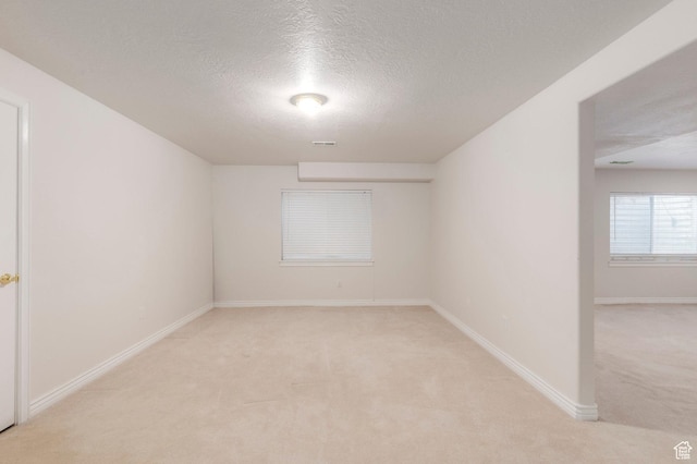 unfurnished room with light colored carpet, baseboards, a textured ceiling, and visible vents