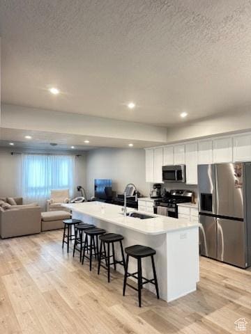 413 S 980 W, American Fork, UT 84003 - kitchen with white cabinets, a kitchen breakfast bar, a sink, a textured ceiling, and appliances with stainless steel finishes