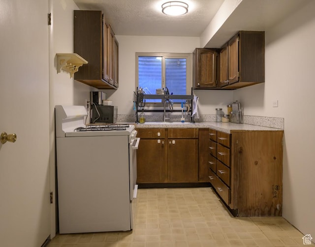 kitchen with light floors, light countertops, a sink, and gas range gas stove