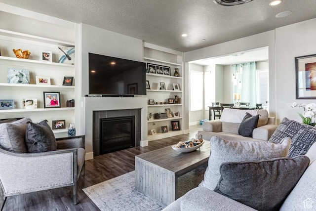 living room featuring dark wood-style floors, a textured ceiling, a glass covered fireplace, recessed lighting, and built in shelves