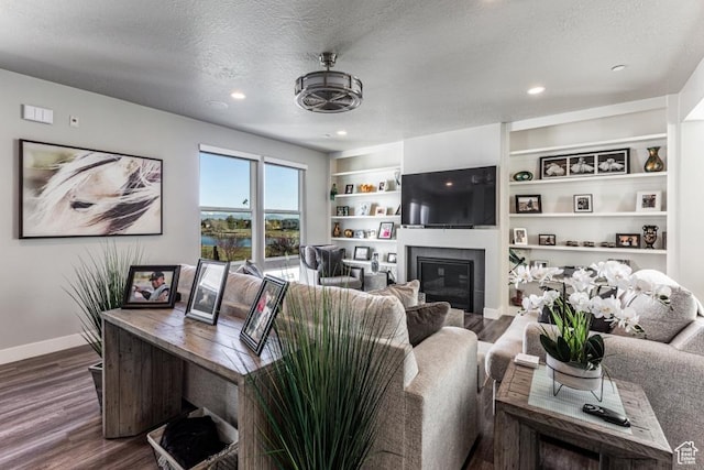 living area featuring wood finished floors, a textured ceiling, a glass covered fireplace, baseboards, and recessed lighting