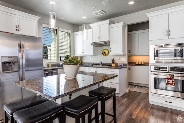 kitchen featuring stainless steel appliances, under cabinet range hood, a kitchen island, and a kitchen bar