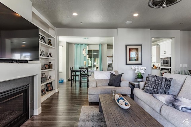living area featuring a textured ceiling, a glass covered fireplace, baseboards, dark wood-style floors, and recessed lighting