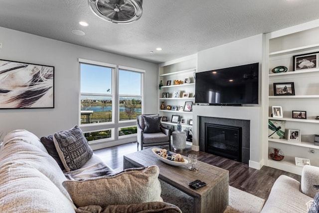 living room featuring wood finished floors, a textured ceiling, built in features, a fireplace, and recessed lighting